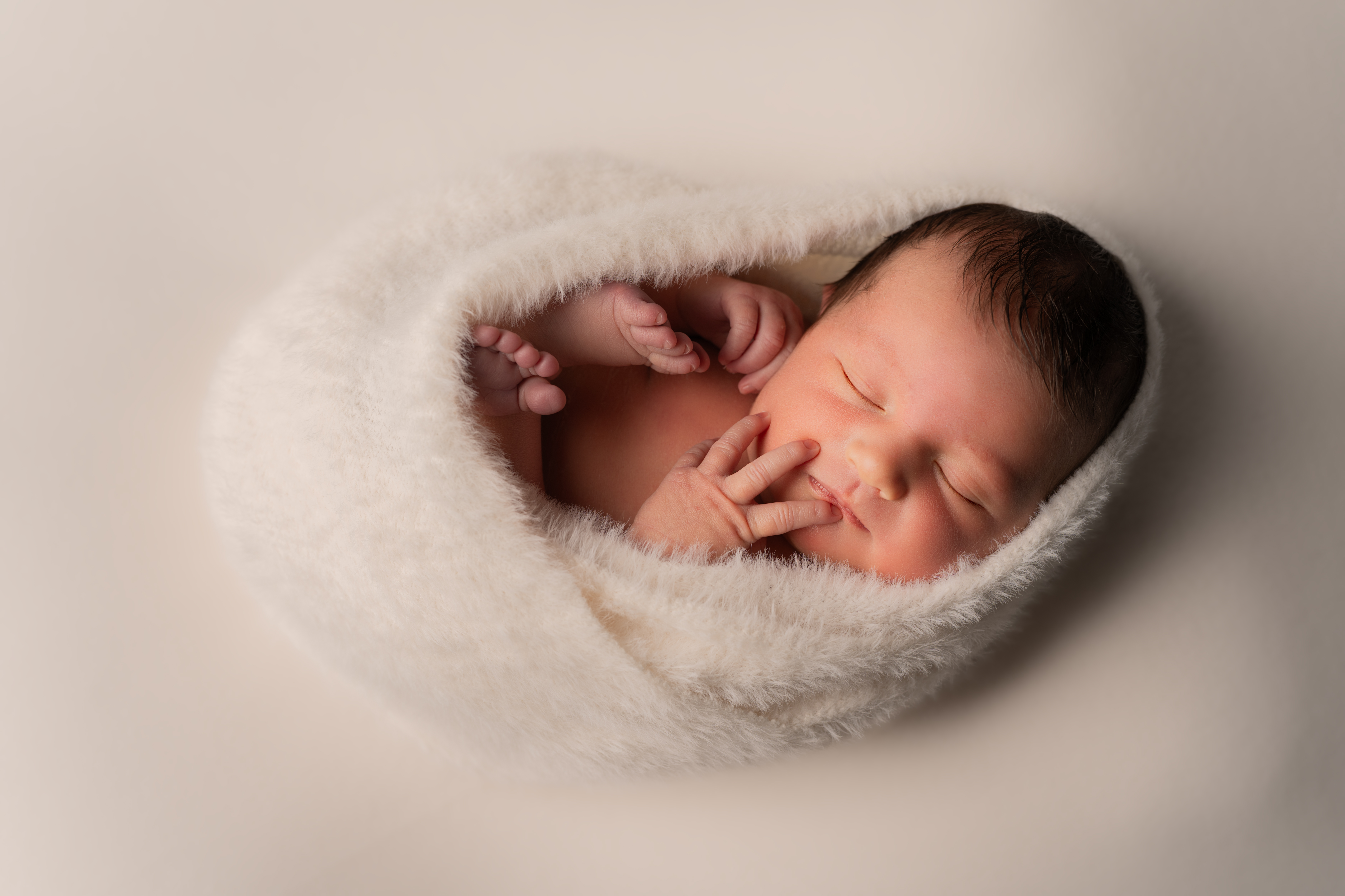 Sleeping newborn wrapped in a soft cream blanket, photographed by Jess
