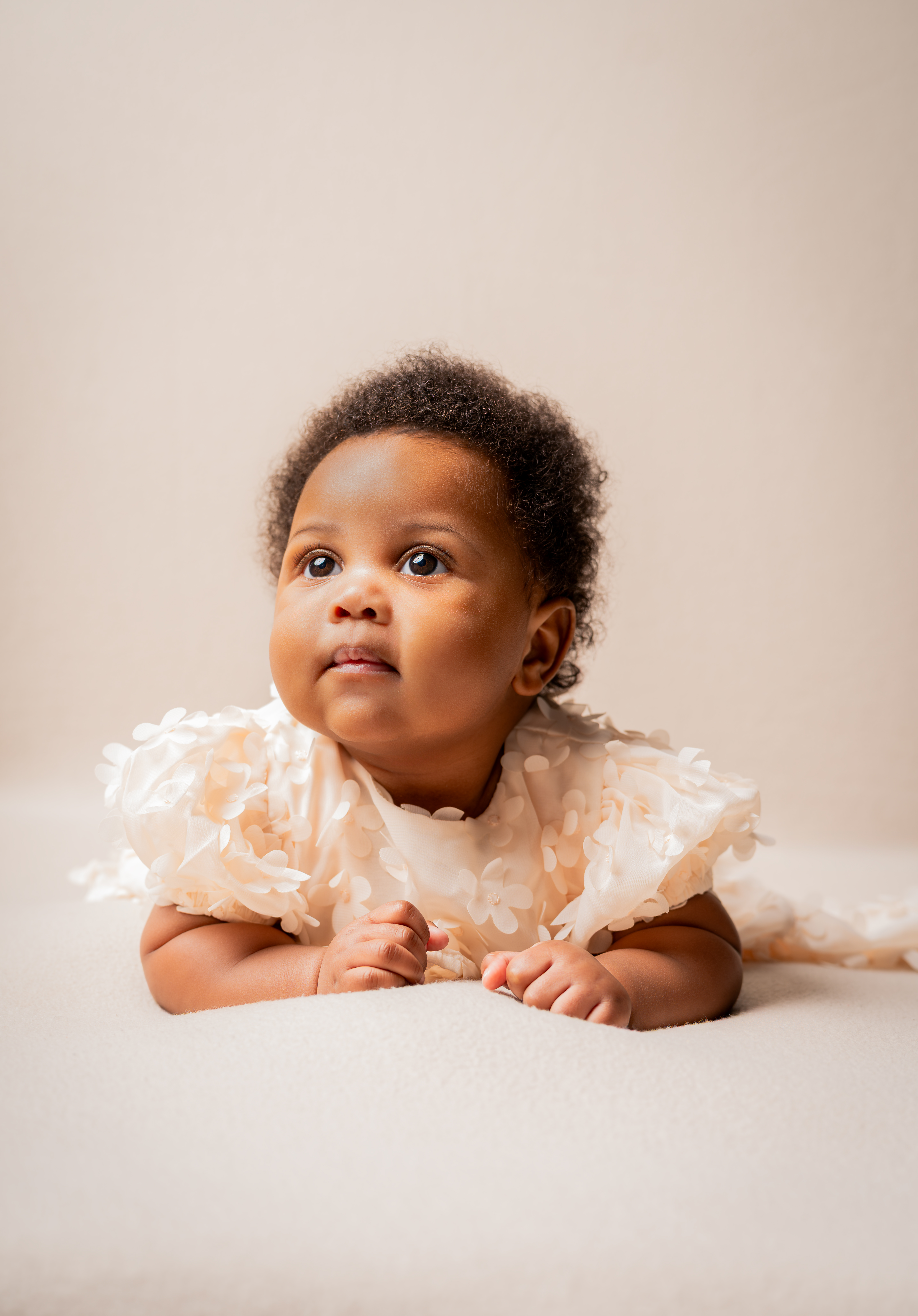 Baby in a cream dress looking up during a studio portrait session